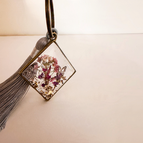 Meadow Butterfly resin bag charm with pressed pink and purple flowers in a bronze frame and grey tassel