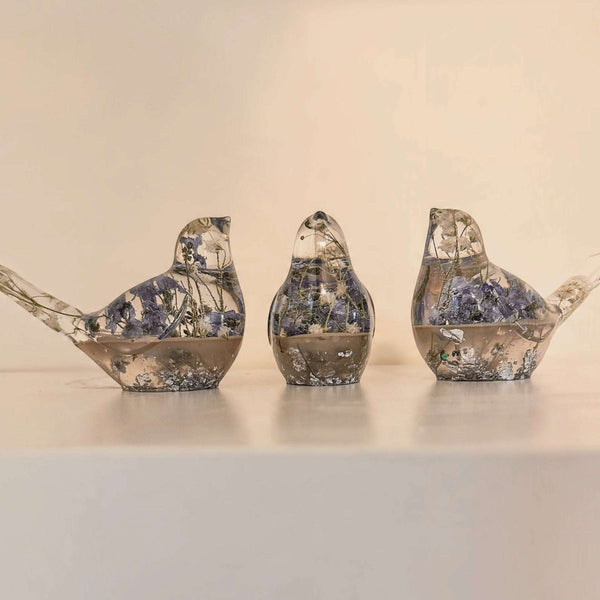 Memorial resin bird with ashes shown as three clear resin songbirds with blue flowers and metallic gold flecks