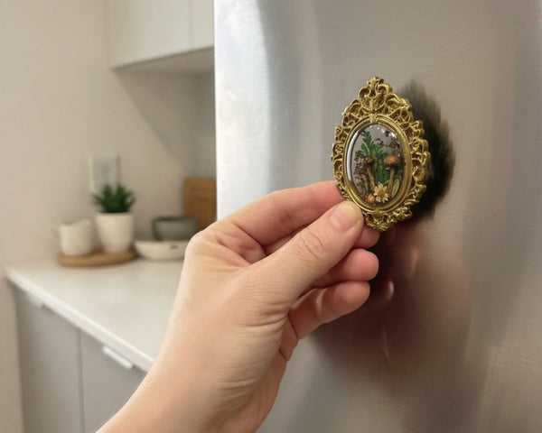 Mushroom fridge magnet held in hand to show its 2.5 inch size against a stainless steel fridge