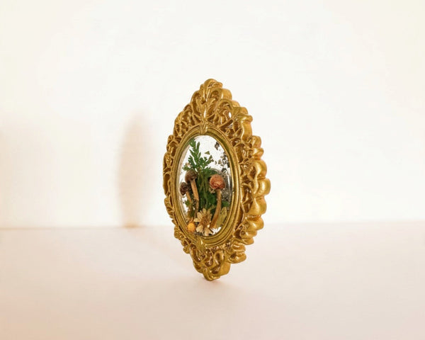 Mushroom fridge magnet standing upright in its ornate gold frame against a soft white background