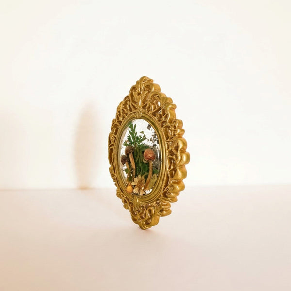Mushroom fridge magnet standing upright in its ornate gold frame against a soft white background