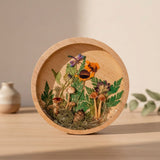 mushroom trinket dish in a round natural wood rim with clear resin, raised mushrooms, moss, ferns and bright flowers