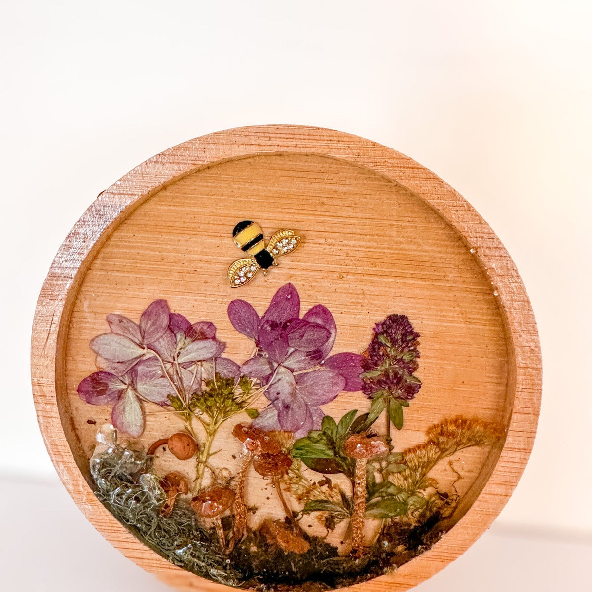 mushroom trinket dish in a round natural wood tray with clear resin, preserved purple flowers, moss and bee charm