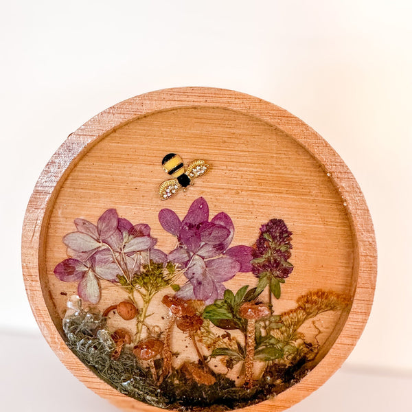mushroom trinket dish in a round natural wood tray with clear resin, preserved purple flowers, moss and bee charm