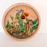 mushroom trinket dish with a natural wood rim, clear resin, raised mushrooms, green ferns, orange flowers and a dragonfly