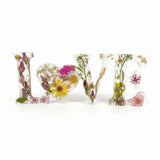 Wild Rose LOVE Word Art in clear resin, featuring pressed pink and white flowers, yellow daisies, greenery, and a heart-shaped O.