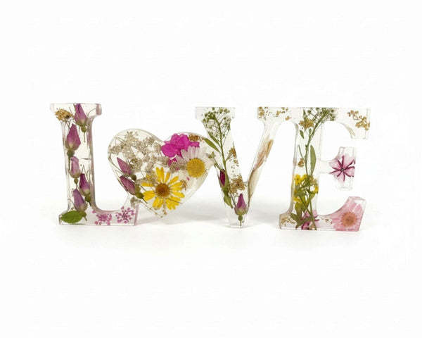 Wild Rose LOVE Word Art in clear resin, featuring pressed pink and white flowers, yellow daisies, greenery, and a heart-shaped O.