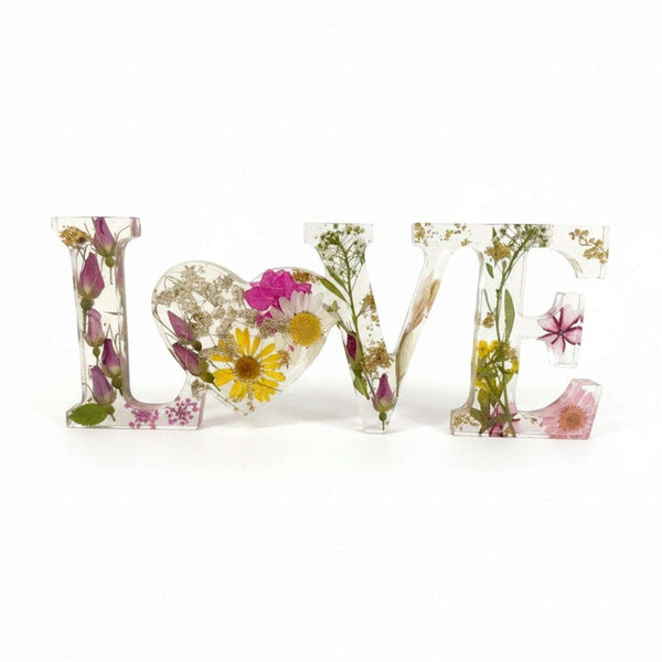 Wild Rose LOVE Word Art in clear resin, featuring pressed pink and white flowers, yellow daisies, greenery, and a heart-shaped O.
