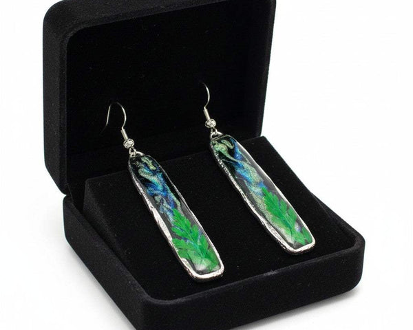 Long silver organic-edged earrings featuring a black and shimmering Northern Lights resin sky with a real green fern at the base.