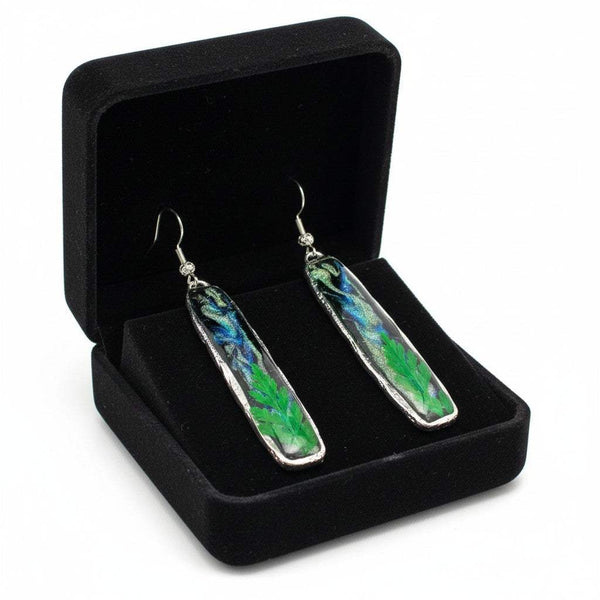 Long silver organic-edged earrings featuring a black and shimmering Northern Lights resin sky with a real green fern at the base.