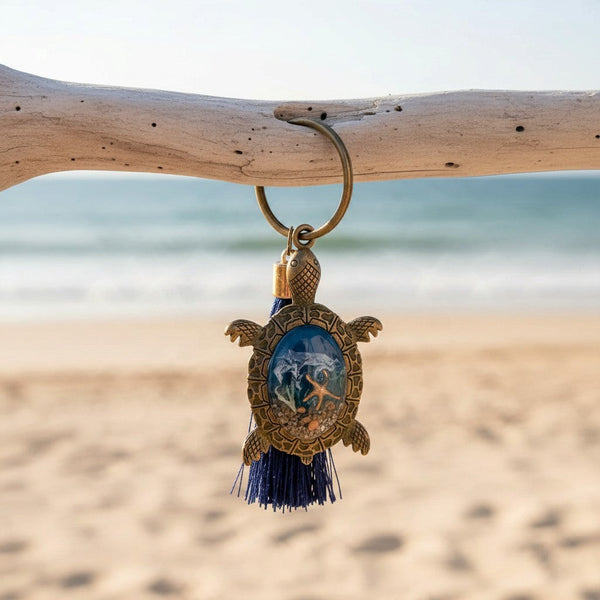 Ocean Keeper sea turtle keychain in bronze-tone metal with a blue resin shell, tiny coastal details and navy tassel