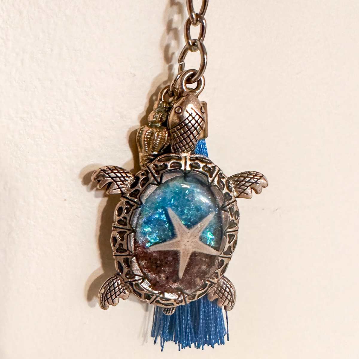 Ocean Keeper sea turtle keychain with antique bronze metal shell frame, blue resin, starfish centerpiece and blue tassel