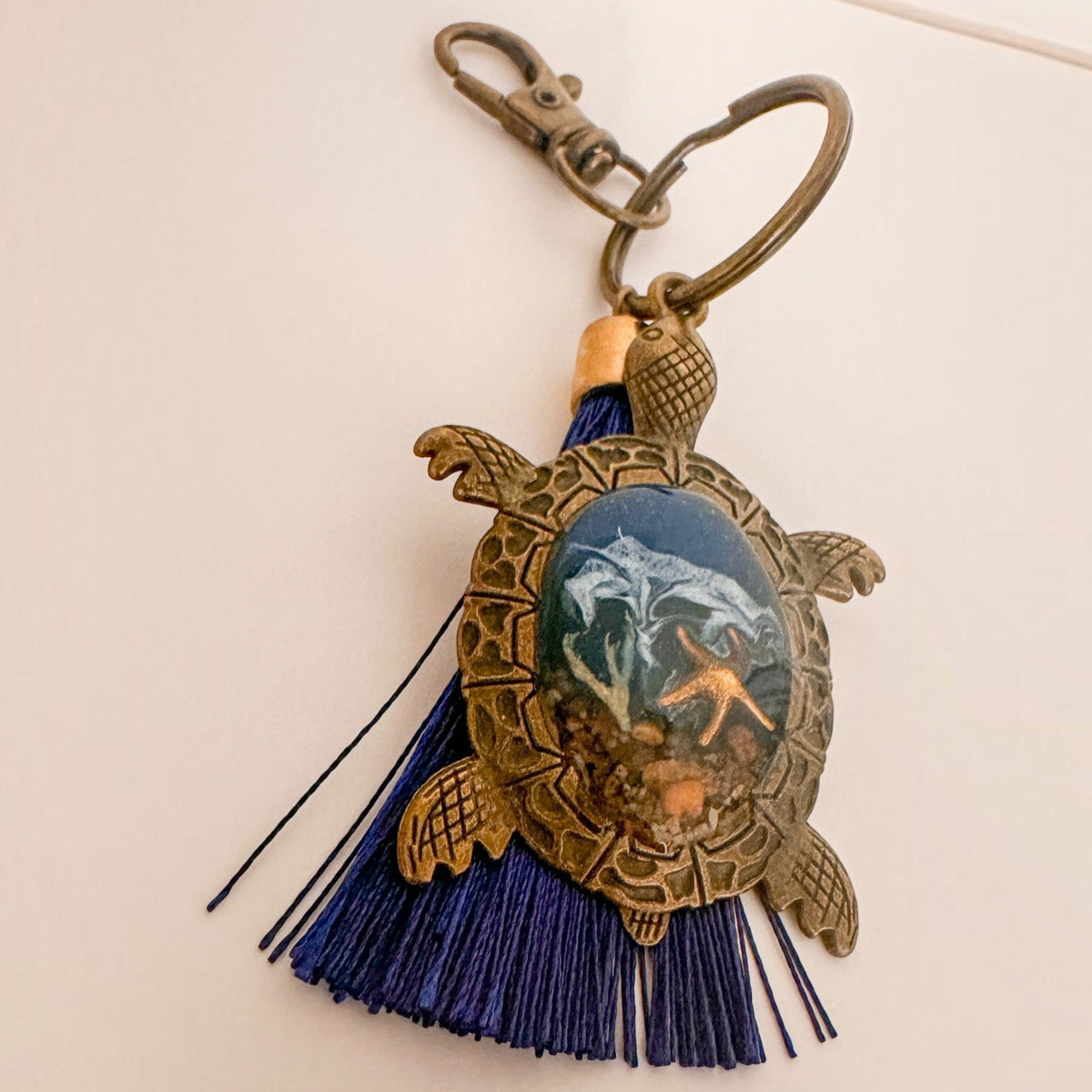 Ocean Keeper sea turtle keychain with antique bronze metal shell frame, ocean-toned resin center and deep blue tassel