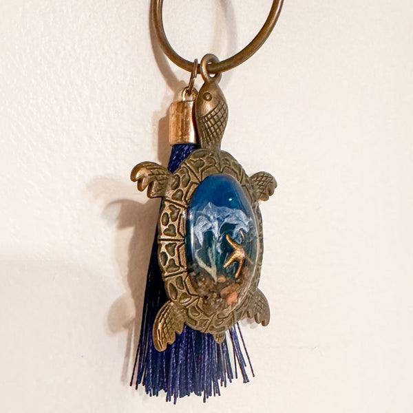 Ocean Keeper turtle keychain in antique bronze metal with a glossy blue resin shell, dark tassel and coastal charms