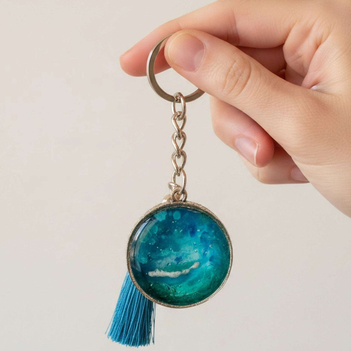 Glow in the dark ocean keychain with layered teal and blue resin, white wave detail, ornate silver frame and blue tassel.
