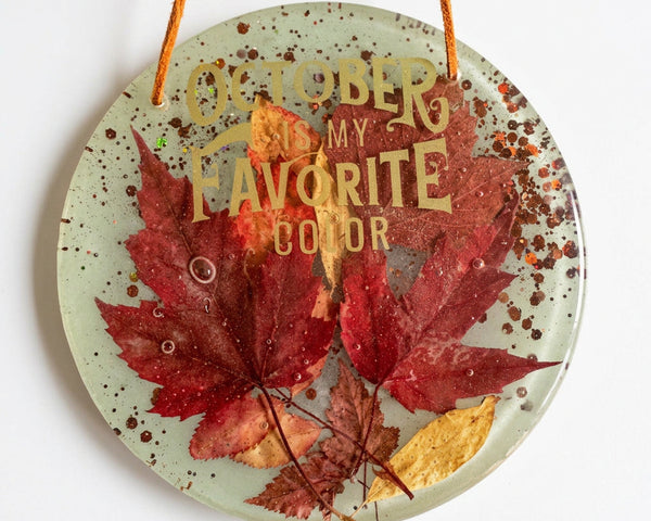 October Glow round resin wall art with red and yellow maple leaves, copper glitter, and gold lettering