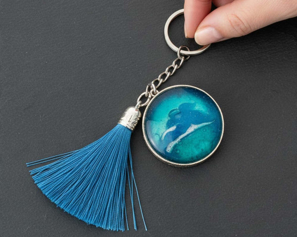 Glow in the dark ocean keychain with layered blue resin, white wave detail, silver frame and blue tassel.