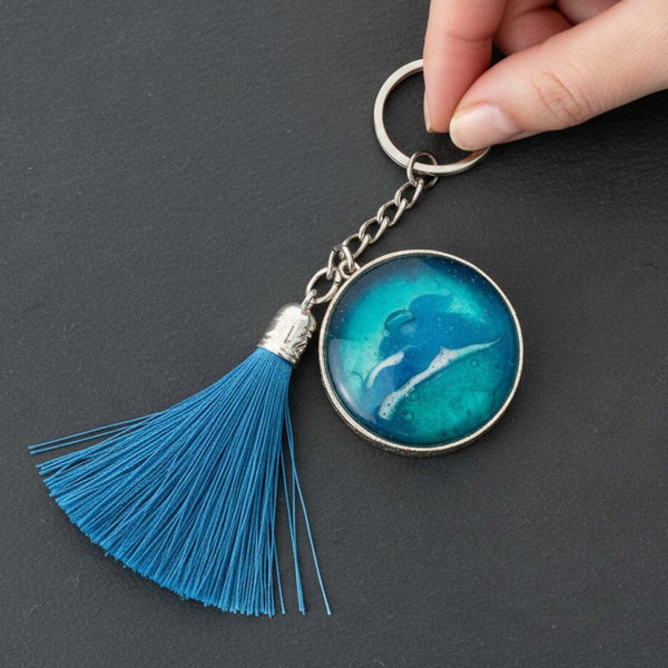 Glow in the dark ocean keychain with layered blue resin, white wave detail, silver frame and blue tassel.
