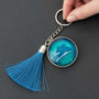 Glow in the dark ocean keychain with layered blue resin, white wave detail, silver frame and blue tassel.
