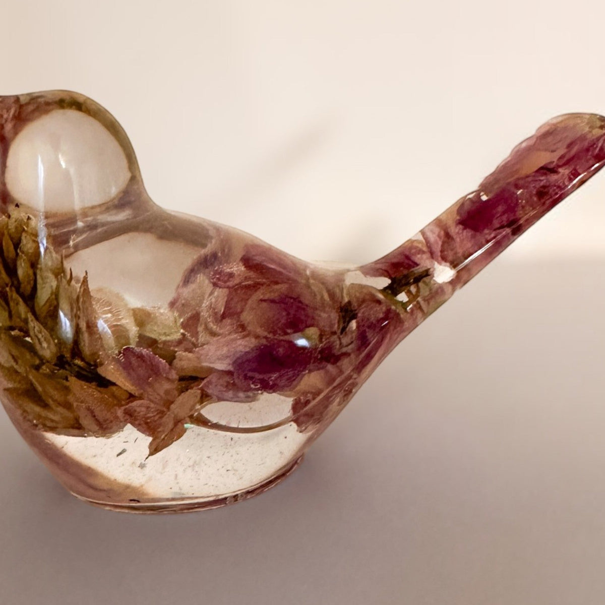 Pink lupine resin bird figurine in clear glossy resin, with dried pink and brown flowers embedded throughout its body and tail.