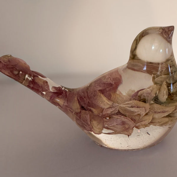 Pink lupine resin bird figurine in clear glossy resin, with dried rose-pink petals rising through its body into the crown.