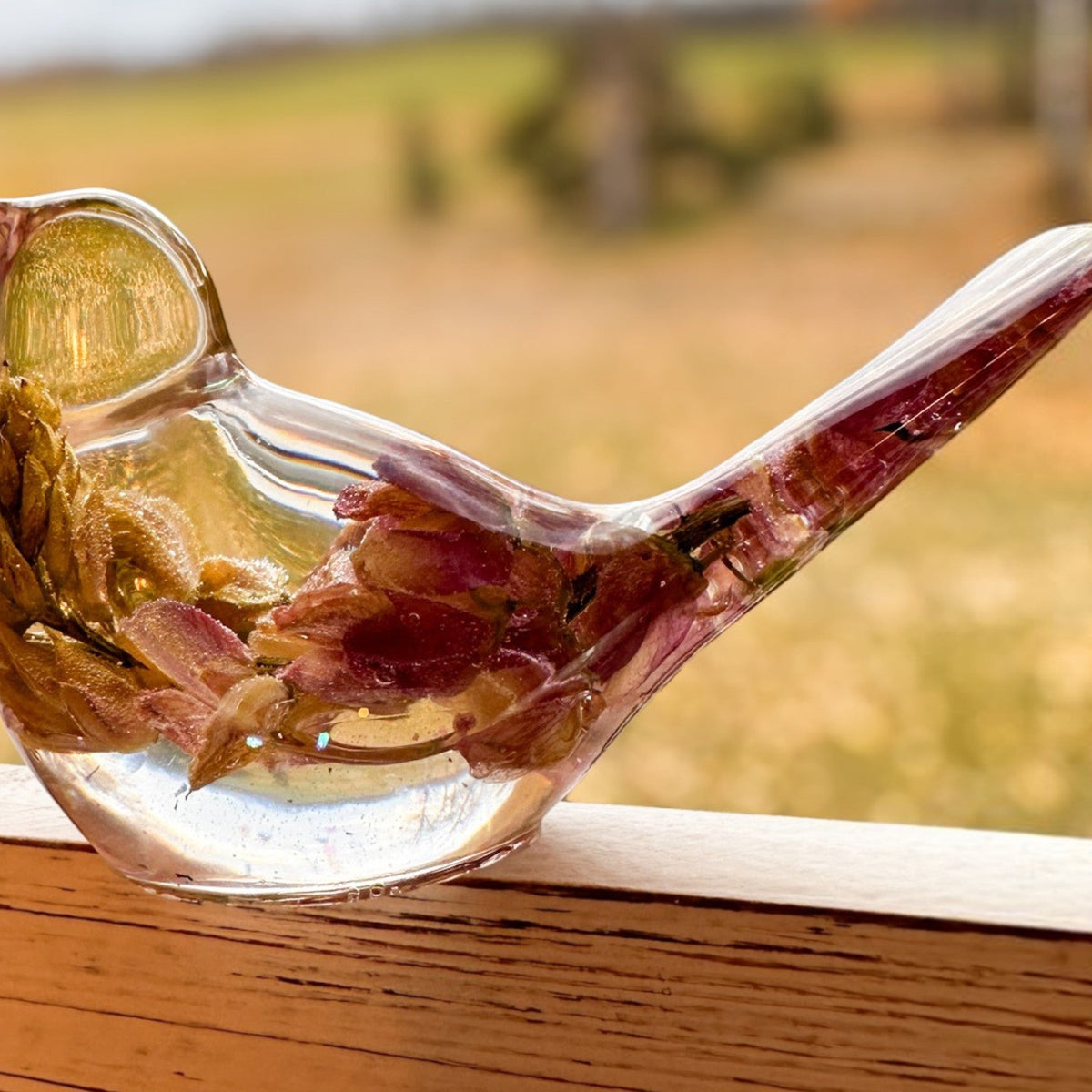 pink lupine resin bird in clear glossy resin, with preserved deep pink petals, gold-toned inclusions and a raised tail.