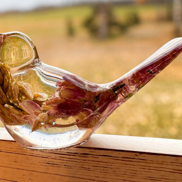 pink lupine resin bird in clear glossy resin, with preserved deep pink petals, gold-toned inclusions and a raised tail.