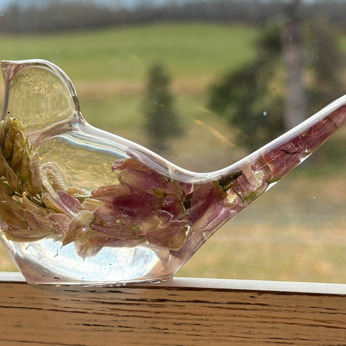 Pink lupine resin bird figurine in clear glossy resin, with a dried pink flower rising through its body and pointed tail.