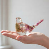 Pink lupine resin bird figurine in clear glossy resin, with preserved pink and cream flowers and a raised tail.