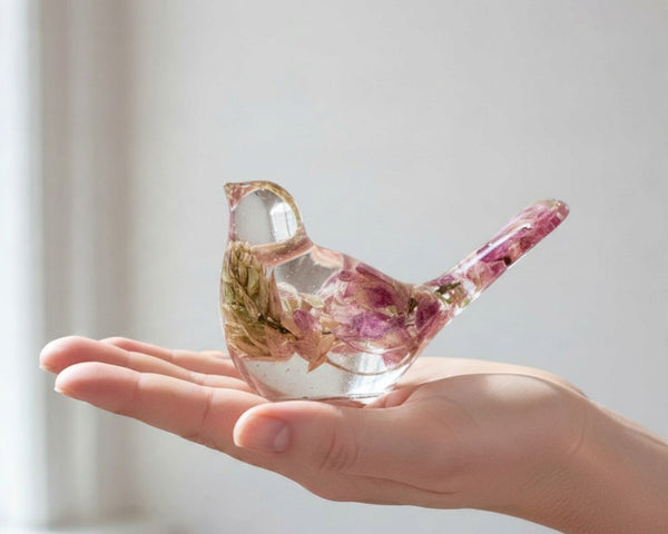 Pink lupine resin bird figurine in clear glossy resin, with preserved pink and cream flowers and a raised tail.