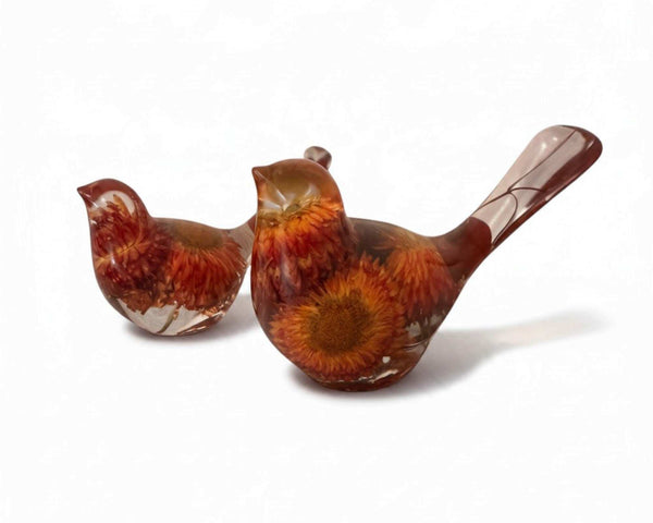 Resin Bird Pair with amber-clear bodies, rust-red and orange dried flowers, and long sculpted tails.