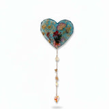 Glow in the dark heart suncatcher in blue resin with pressed wildflowers, gold leaf, and a gold chain with crystal drops and charms.