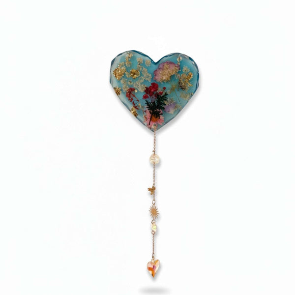 Glow in the dark heart suncatcher in blue resin with pressed wildflowers, gold leaf, and a gold chain with crystal drops and charms.