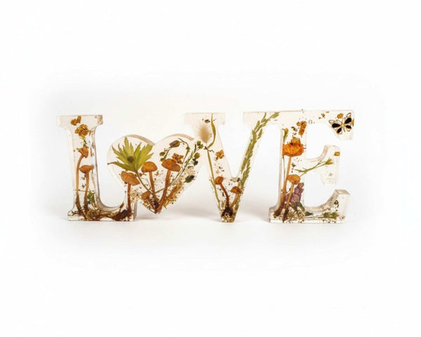 Resin mushroom decor spelling LOVE in clear resin, with dried mushrooms, ferns, moss, gold flecks and butterfly charm