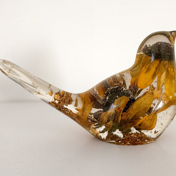 Black eyed susan resin bird with clear glossy body, golden petals, dark brown flower centres and gold leaf accents along its tail and base.