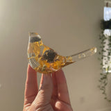 black eyed susan resin bird in clear resin with amber-yellow dried flowers, dark centres, and gold leaf accents along its tail and base
