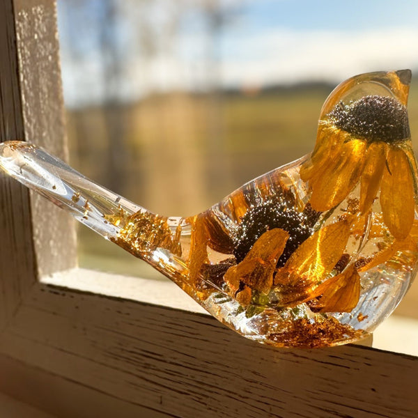 Black eyed susan resin bird in clear resin, with golden layered petals, dark centres and gold leaf accents along the tail and base.