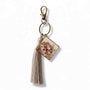 Pressed flower resin bag charm with clear square resin, pink and purple pressed blooms, bronze hardware and a grey tassel.