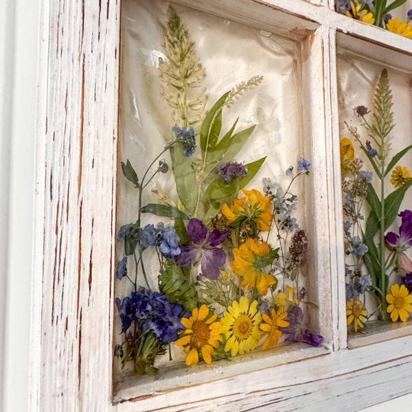Pressed flower window art with yellow daisies and purple violets along the lower panes