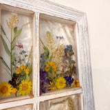 Corner detail of the pressed flower window art and its white distressed wood frame
