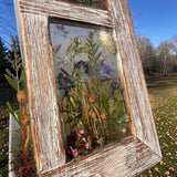 Pressed flower window art in a weathered whitewashed wood frame, with translucent resin and colorful preserved botanicals