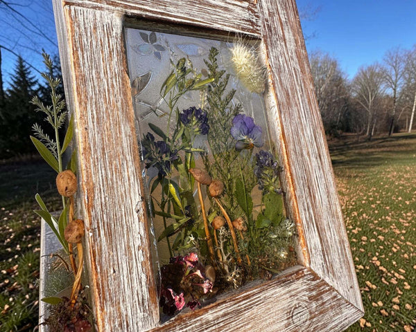 Pressed flower window art in a weathered whitewashed wood frame, with translucent resin and colorful preserved botanicals