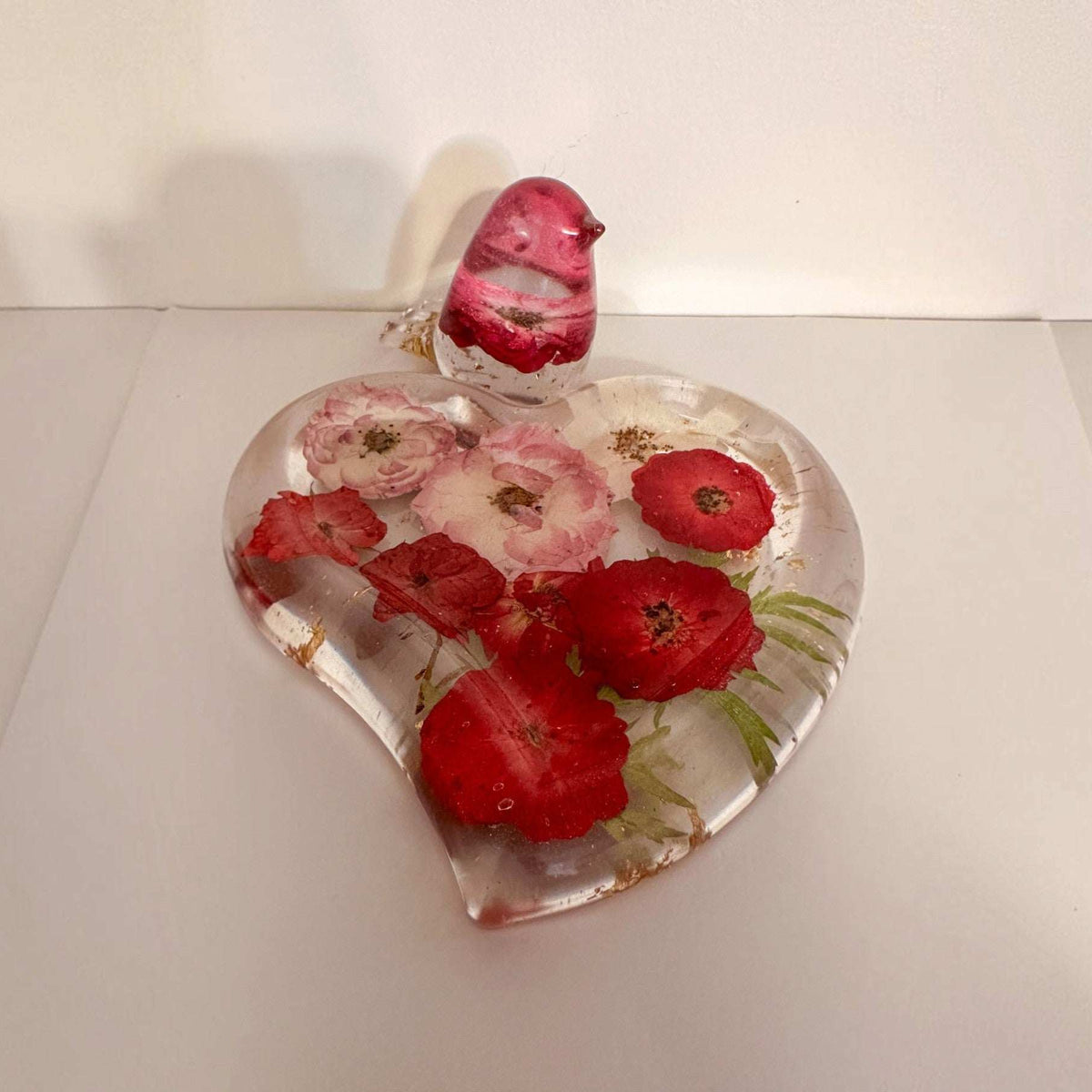 Rose heart trinket dish in clear resin with pressed red and pink flowers, green leaves, gold flecks and a matching bird