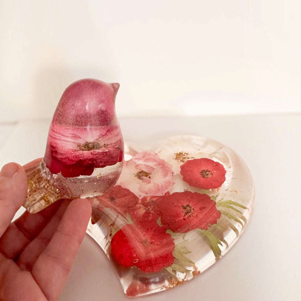 rose heart trinket dish in clear resin with pressed red and pink roses and green leaves, paired with a rose-filled songbird