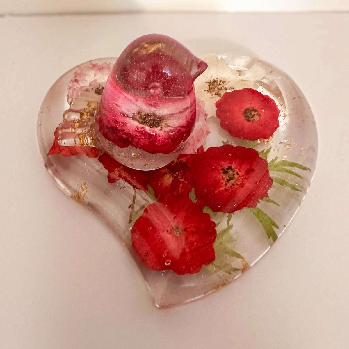 rose heart trinket dish in clear resin with pressed red roses, green botanical accents, gold leaf and a matching rose-filled bird