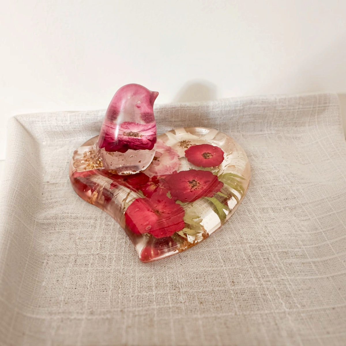 Rose heart trinket dish in clear resin with red and pink pressed flowers, green accents, gold leaf, and a matching pink bird