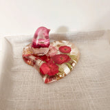 Rose heart trinket dish in clear resin with red and pink pressed flowers, green accents, gold leaf, and a matching pink bird
