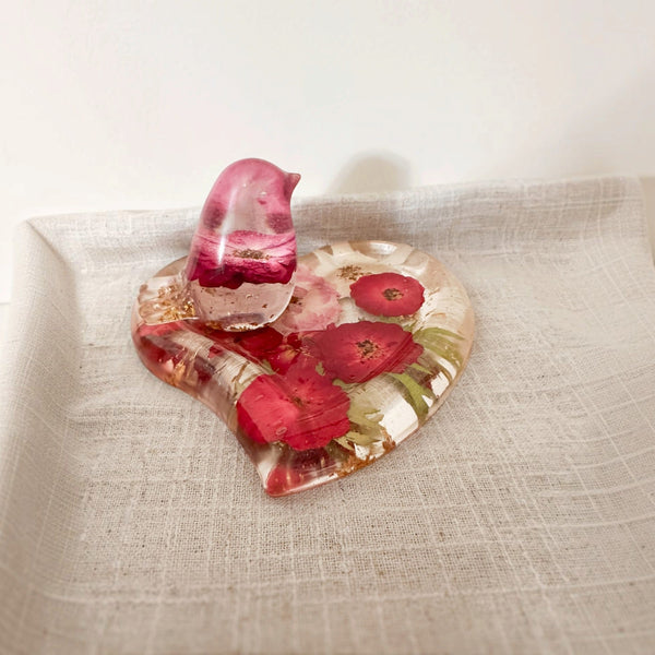 Rose heart trinket dish in clear resin with red and pink pressed flowers, green accents, gold leaf, and a matching pink bird