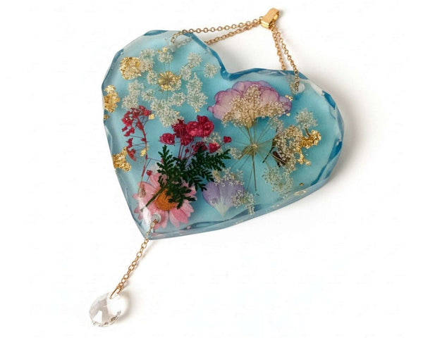 Glow in the dark heart suncatcher handcrafted in blue resin with real pressed wildflowers, gold leaf, and a crystal drop.