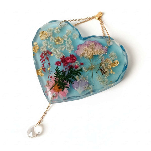 Glow in the dark heart suncatcher handcrafted in blue resin with real pressed wildflowers, gold leaf, and a crystal drop.